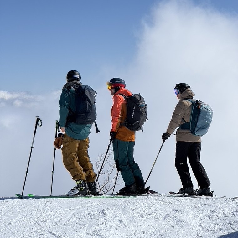 Three skiers on a ridge above the clouds